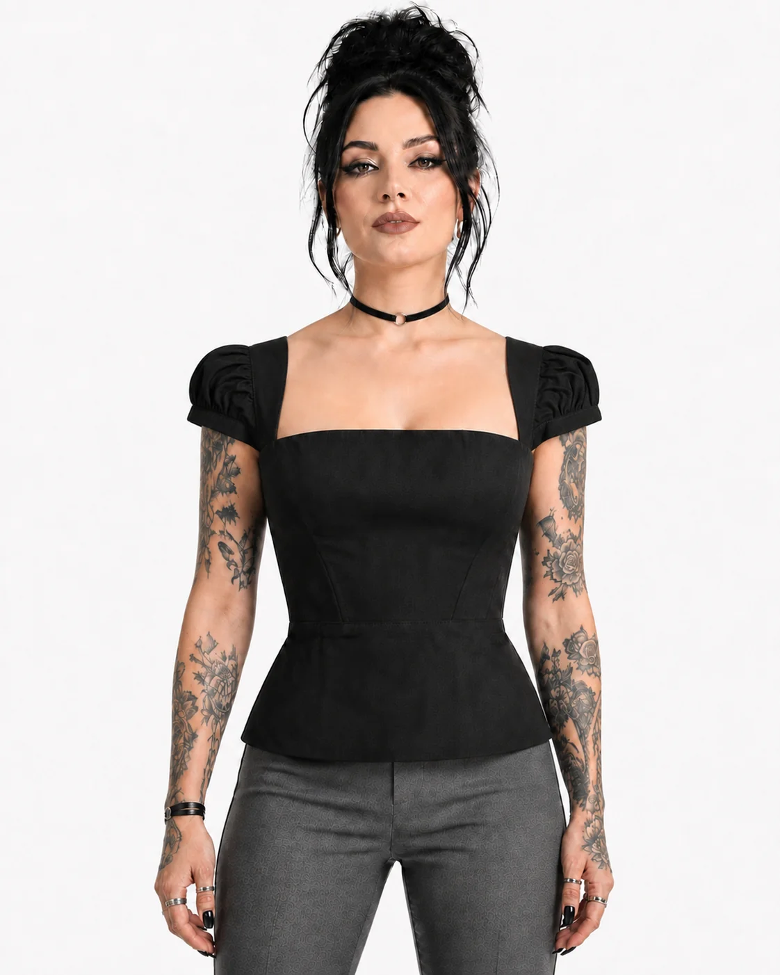 A woman modeling a black puff-sleeve square-neck top with a peplum waist, paired with gray pants, against a plain white background.