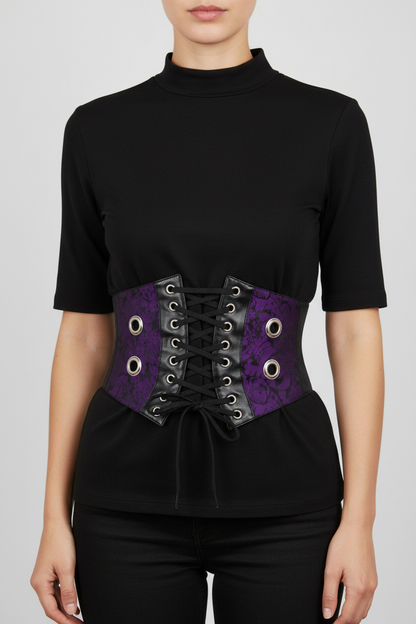 A model wearing a black short-sleeve mock neck top and black pants, featuring a wide purple lace-up waist belt with black patterned panels and silver grommets.
