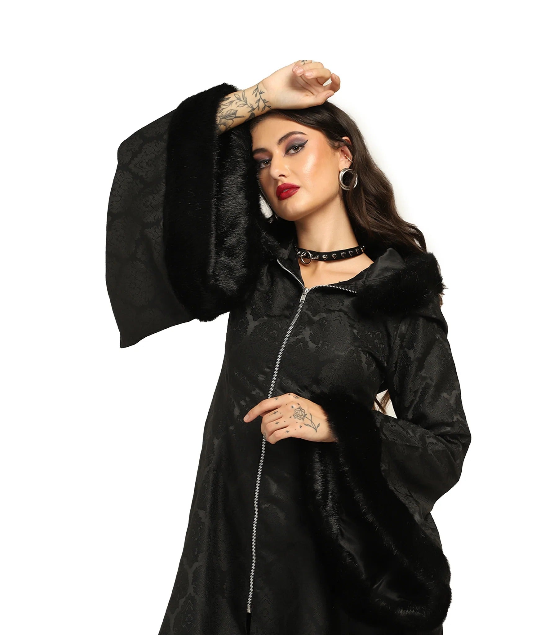A woman modeling a black long-sleeved coat with wide bell sleeves, a black faux-fur collar, and a silver zipper, set against a plain white background.