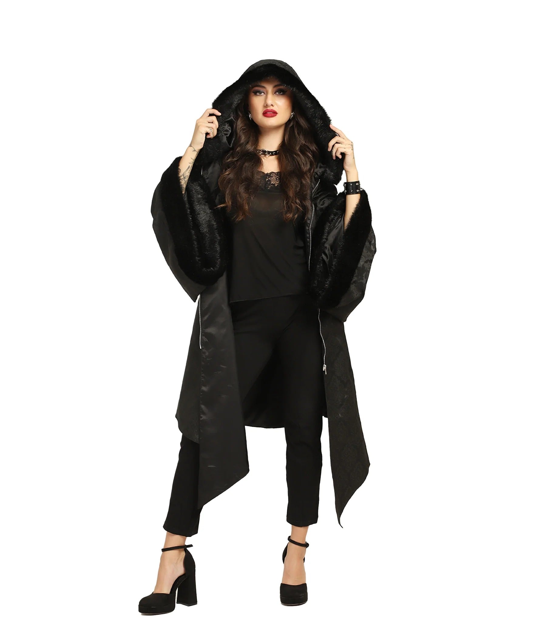 Woman wearing a black brocade hooded Gothic coat with fur trim at the hood and sleeves and an uneven pointed hem.